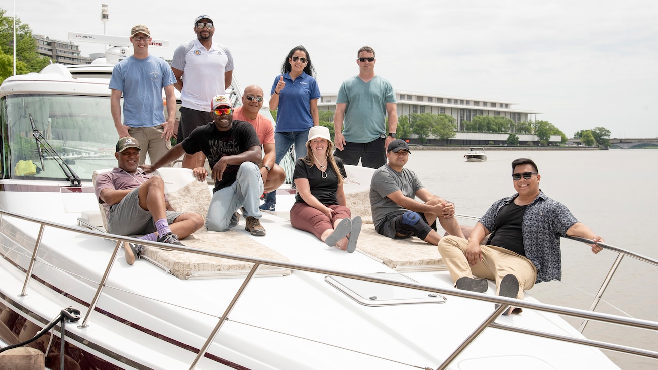 Participants of the fishing trip pose for a group shot on the bow of the boat with the Kennedy Center in the background.