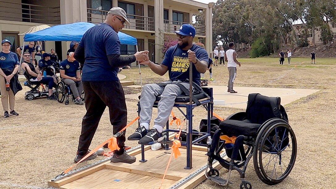 An athlete practices shot put from a throwing chair with his wheelchair nearby,