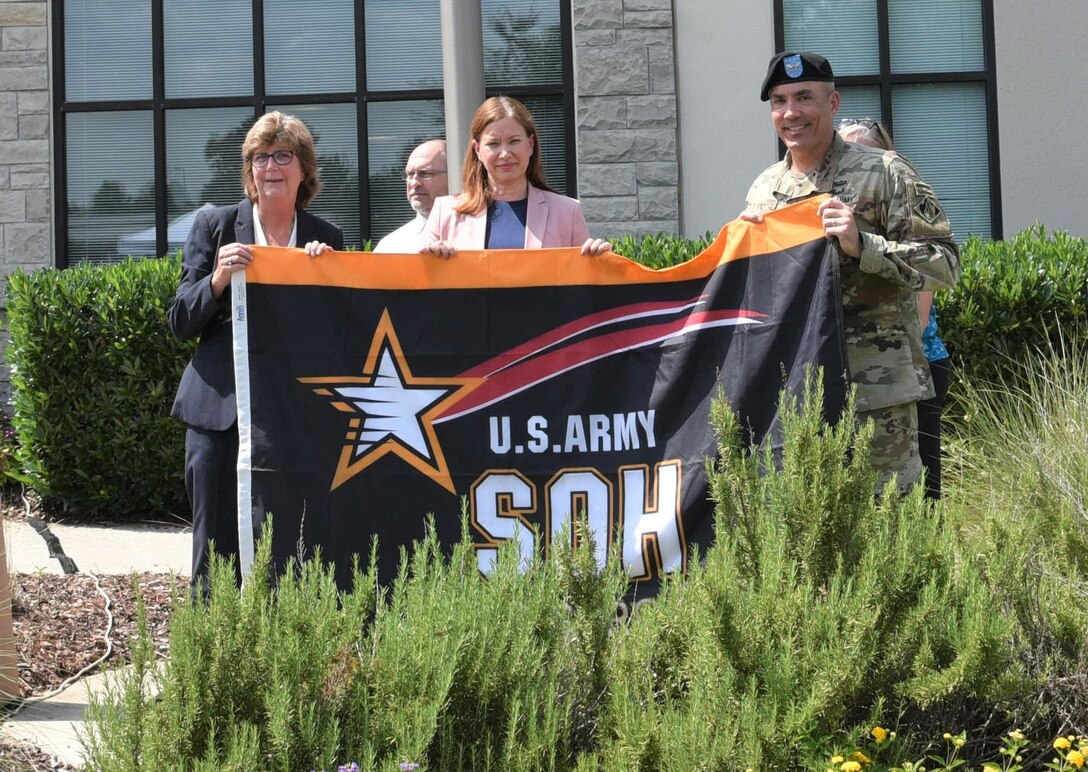 Kellie Williams, Huntsville Center safety manager; Amy Borman, deputy assistant secretary of the Army for Environment, Safety and Occupational Health; and Col. Sebastien P. Jolie, Huntsville Center commander, hold up the Army Safety and Occupational Health flag during an award ceremony June 15. The U.S. Army Engineering and Support Center, Huntsville received the Army's Safety and Occupational Health Star, making the organization the first in the Corps of Engineers to earn the award. (Photo by Elizabeth Canfil)