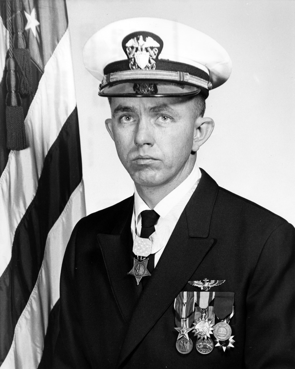 A man in a military dress uniform and cap wears a medal around his neck.