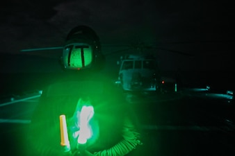 Aviation Technician Airman Holden Holland, from Atlanta, signals as the nighttime aircraft handling officer for an MH-60R Sea Hawk helicopter assigned to the "Raptors" of Helicopter Maritime Strike Squadron (HSM) 71 aboard the Ticonderoga-class guided-missile cruiser USS Mobile Bay (CG 53).