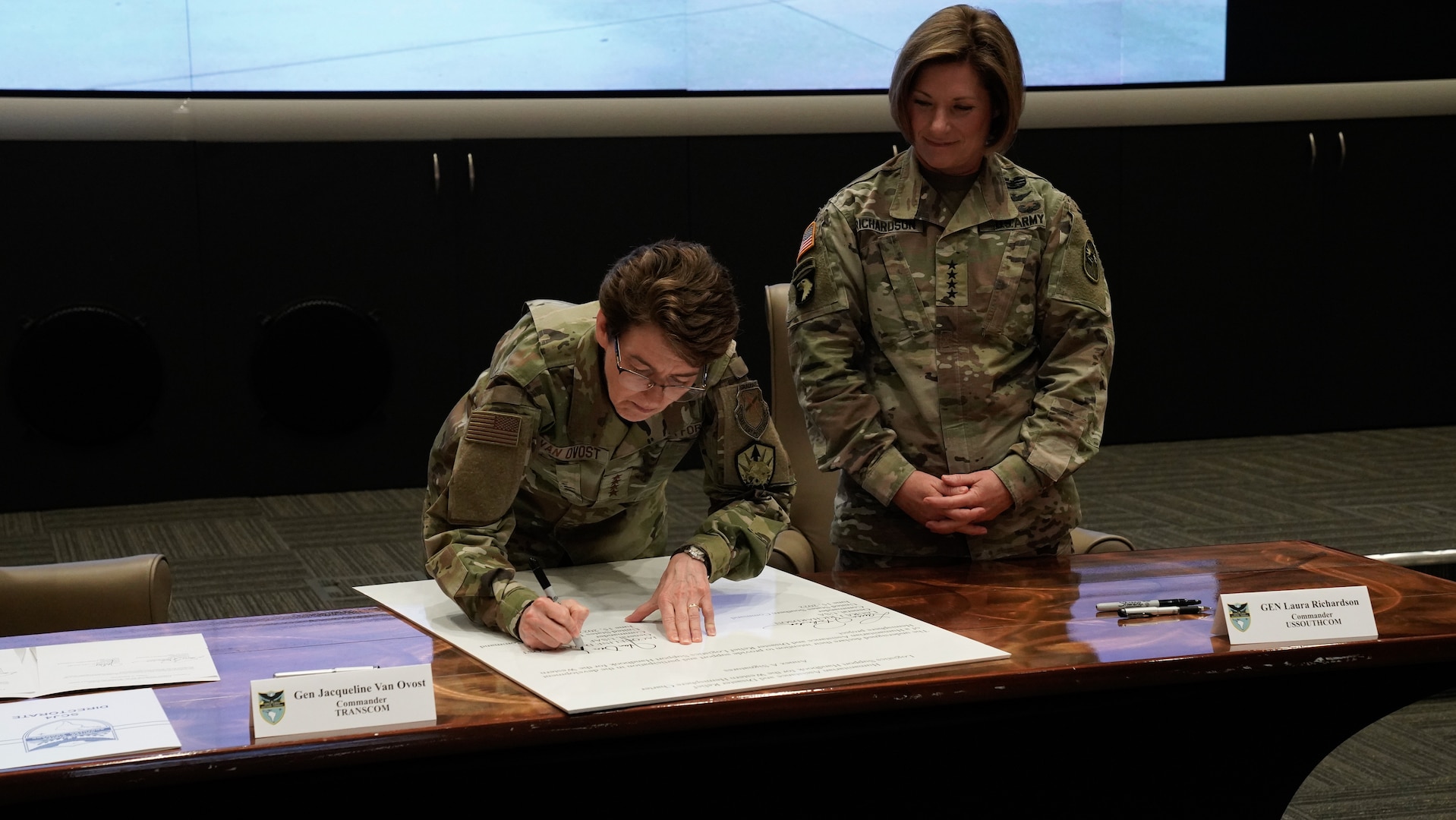 A woman signs a document as another woman looks on.