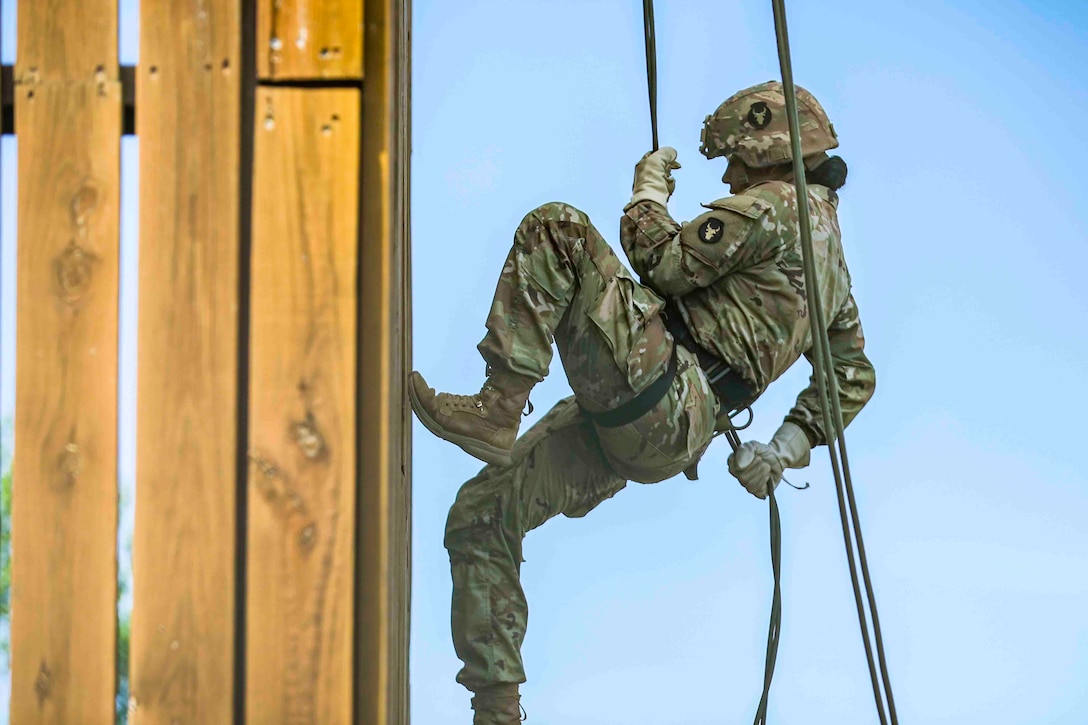 A soldier rappels down a wall.