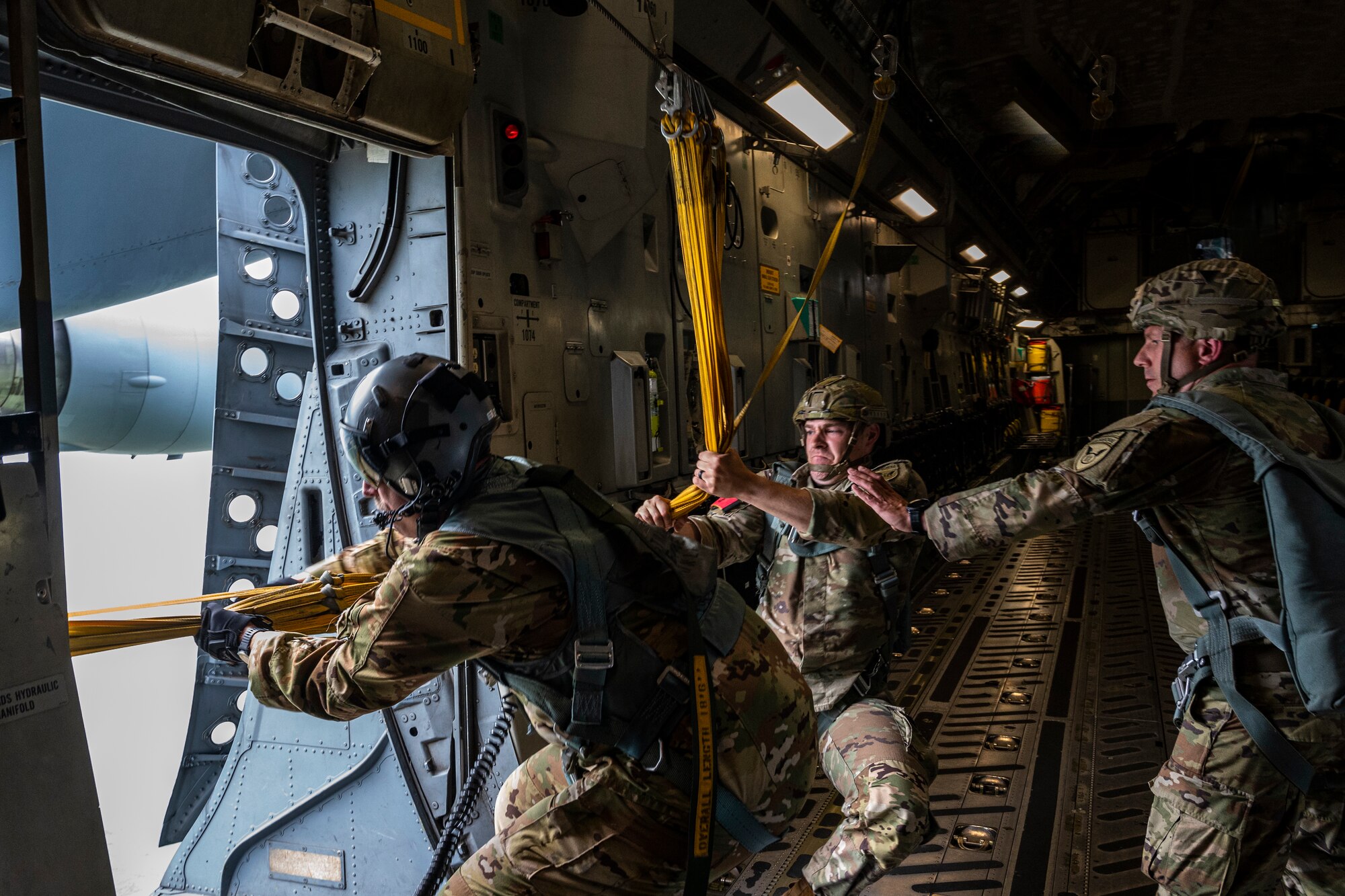 U.S. Air Force Master Sgt. Norman Metz, 517th Airlift Squadron loadmaster and U.S. Army jumpmasters, pull static lines back into the aircraft over Allen Army Airfield, Fort Greely, June 15, 2022 during RED FLAG-Alaska 22-2.  The static line is a cord attached at one end of the aircraft and at the other to the paratrooper’s parachute container. RF-A provides realistic combat training by integrating joint, coalition and multilateral forces into simulated forward operating bases. (U.S. Air Force photo by Sheila deVera)