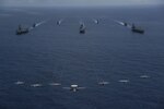 PHILIPPINE SEA (June 12, 2022) Aircraft from Carrier Air Wing (CVW) 9 fly over the Nimitz-class aircraft carrier Abraham Lincoln (CVN 72), front left, America-class amphibious assault ship USS Tripoli (LHA 7), front center, Nimitz-class aircraft carrier USS Ronald Reagan (CVN 76), front right, Ticonderoga-class guided-missile cruiser USS Mobile Bay (CG 53), middle left, Arleigh Burke-class guided-missile destroyer USS Benfold (DDG 65), middle center, Ticonderoga-class guided-missile cruiser USS Antietam (CG 54), middle right, Arleigh Burke-class guided-missile destroyer USS Spruance (DDG 111), back left, and Arleigh Burke-class guided-missile destroyer USS Fitzgerald (DDG 62), back right, as they sail in formation during Valiant Shield 2022 (VS22). VS22 is a U.S.-only, biennial field training exercise (FTX) focused on integration of joint training in a multi-domain environment. This training builds real-world proficiency in sustaining joint forces through detecting, locating, tracking, and engaging units at sea, in the air, on land, and in cyberspace in response to a range of mission areas. (U.S. Navy photo by Mass Communication Specialist 3rd Class Thaddeus Berry)
