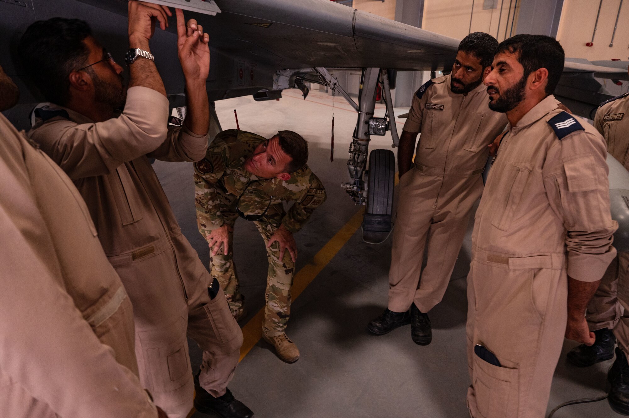 A U.S. Air Force firefighter, center, from the 379th Air Expeditionary Wing, alongside Royal Air Force of Oman Airmen, observe the use of a safety feature on a RAFO Eurofighter Typhoon aircraft during a fire safety brief from a RAFO fire chief at Thumrait Air Base, Oman, May 18, 2022. The RAFO fire chief showcased safety measures that reside under the front edge of the wing of the aircraft. (U.S. Air Force photo by Staff Sgt. Dana Tourtellotte)