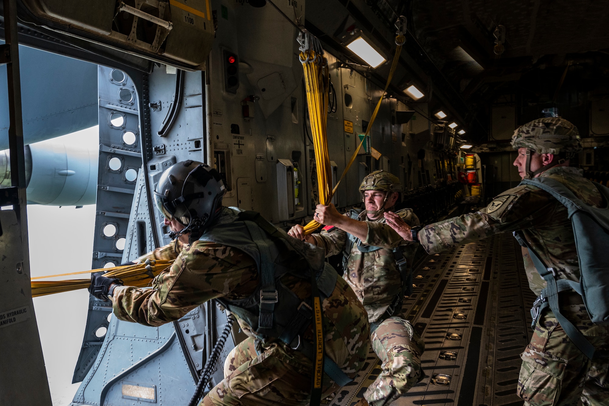 U.S. Air Force Master Sgt. Norman Metz, 517th Airlift Squadron loadmaster and U.S. Army jumpmasters, pull static lines back into the aircraft over Allen Army Airfield, Fort Greely, June 15, 2022 during RED FLAG-Alaska 22-2.  The static line is a cord attached at one end of the aircraft and at the other to the paratrooper’s parachute container. RF-A provides realistic combat training by integrating joint, coalition and multilateral forces into simulated forward operating bases. (U.S. Air Force photo by Sheila deVera)