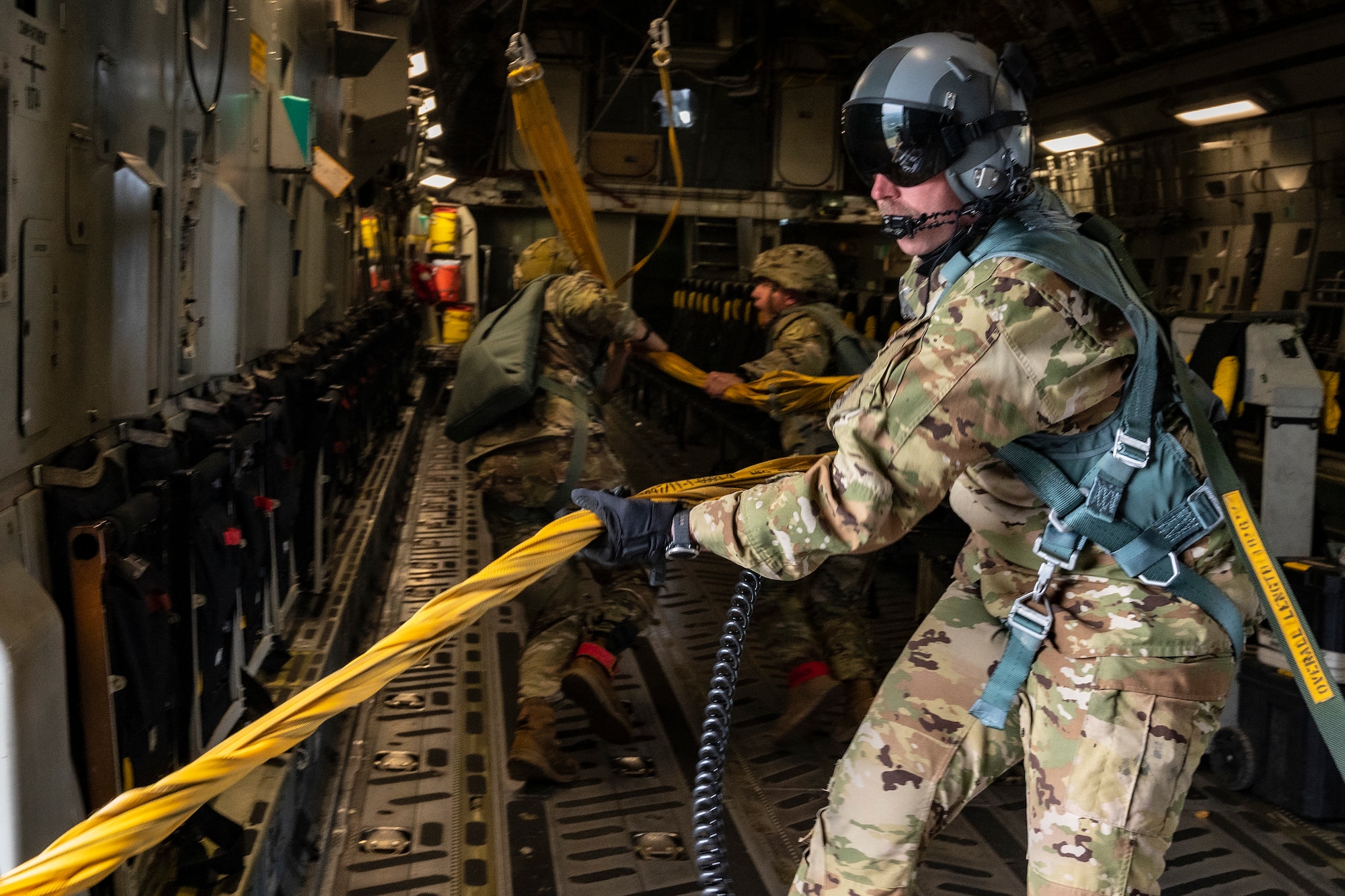 U.S. Air Force Master Sgt. Norman Metz, 517th Airlift Squadron loadmaster and U.S. Army jumpmasters, pull static lines back into the aircraft over Allen Army Airfield, Fort Greely, June 15, 2022 during RED FLAG-Alaska 22-2.  The static line is a cord attached at one end of the aircraft and at the other to the paratrooper’s parachute container. RF-A provides realistic combat training by integrating joint, coalition and multilateral forces into simulated forward operating bases. (U.S. Air Force photo by Sheila deVera)