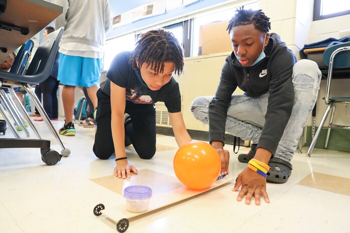 Two middle school students test their balloon buggy to see how far it will go after adding weight to the buggy.