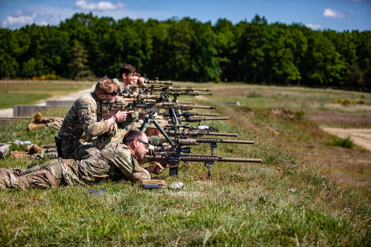 A group of soldiers in kneeling and prone positions fire their rifles and look down their weapons’ sights.