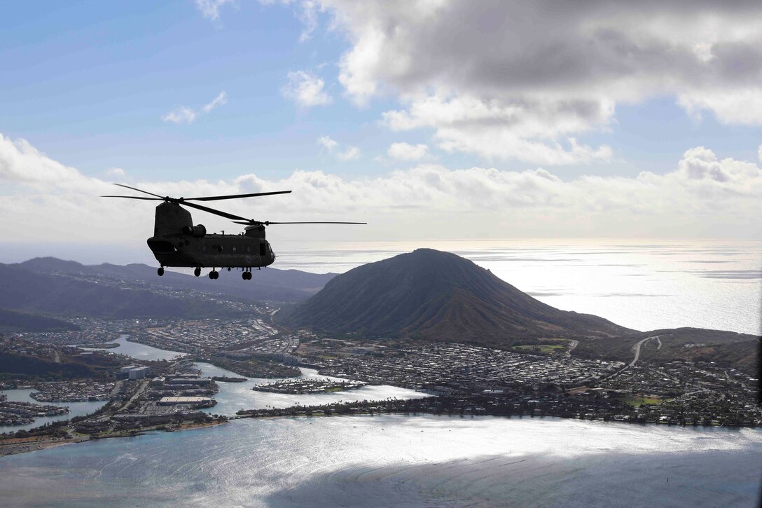 A helicopter flies over water; a mountain can be seen in the background.