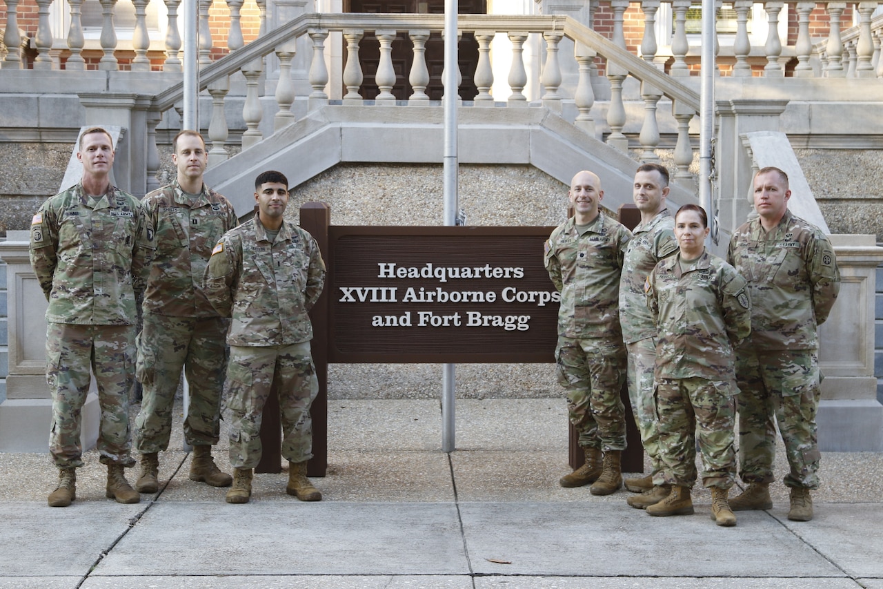 Seven service members pose for a photo next to a sign.