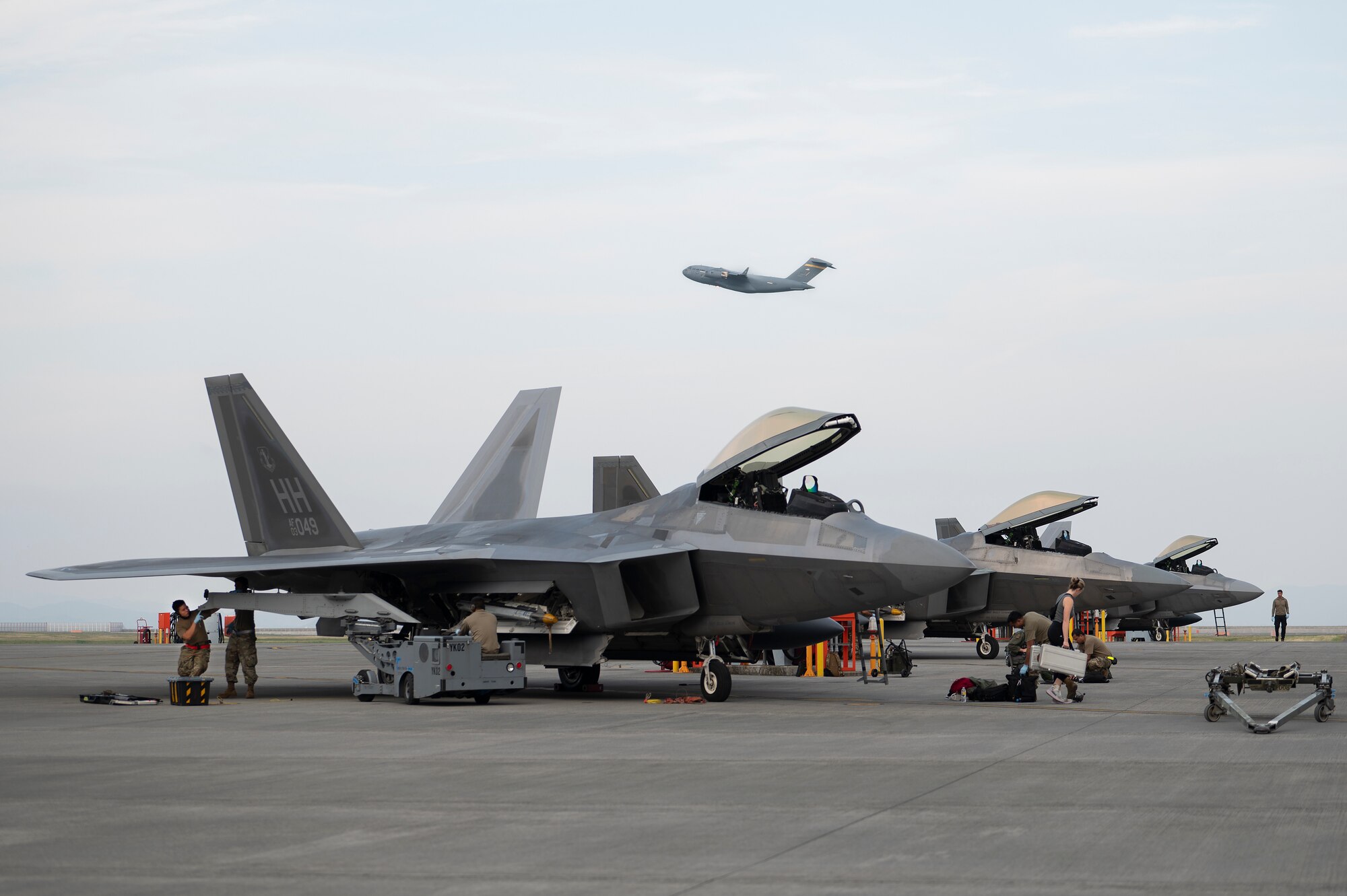 U.S. Air Force F-22 Raptor fighter jets assigned to the 199th Expeditionary Fighter Squadron undergo post-flight procedures as a C-17 Globemaster III transport aircraft takes off from Marine Corps Air Station Iwakuni, Japan, June 15, 2022. The 199th EFS traveled to Iwakuni for an agile combat employment training event, during which the unit is assigned to the 354th Air Expeditionary Wing and integrated with the 356th Expeditionary Fighter Squadron to refine fifth generation integration tactics, techniques and procedures. (U.S. Air Force photo by Staff Sgt. Zade Vadnais)