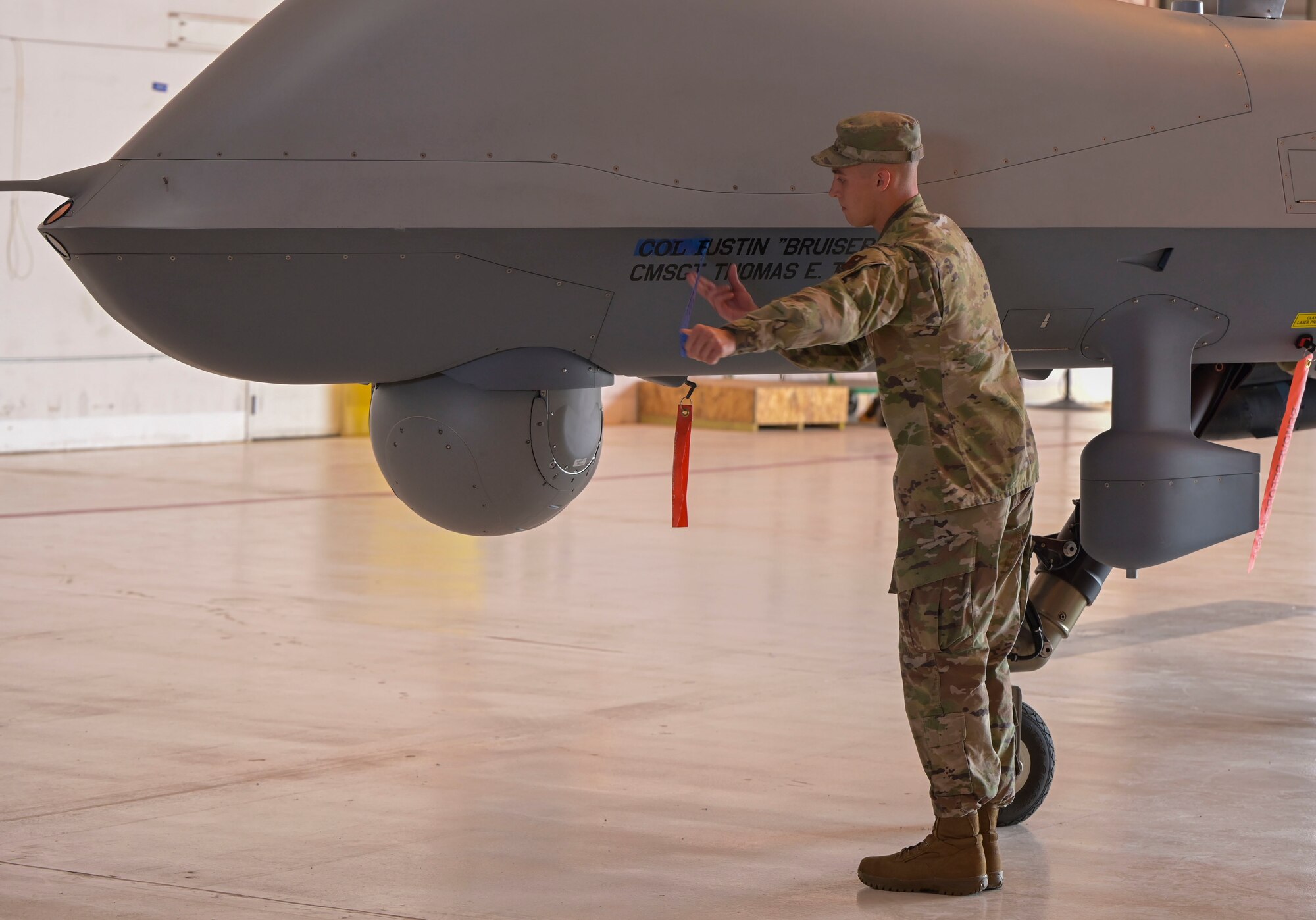 Senior Airman William Watson, 49th Aircraft Maintenance Squadron assistant dedicated crew chief, unveils  the name of Col. Justin B. Spears, 49th Wing commander, name on the 49th Wing MQ-9 Reaper flagship, during a change of command ceremony, June 17, 2022, on Holloman Air Force Base, New Mexico. Holloman is the premier training base for F-16 Viper and MQ-9 Reaper pilots and sensor operators. (U.S. Air Force photo by Airman 1st Class Antonio Salfran)