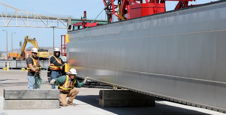 Using hand signals, Jim Young, kneeling, directs the crane operator to lower a stoplog onto a storage area while Chris Lane, holding rope, and Curt White align it. Stoplogs are steel bulkheads used to hold back water during maintenance. The Corps of Engineers removed the stoplogs and opened the MacArthur Lock today after seasonal maintenance and an extended repair. (U.S. Army Corps of Engineers photo by Bill Dowell)