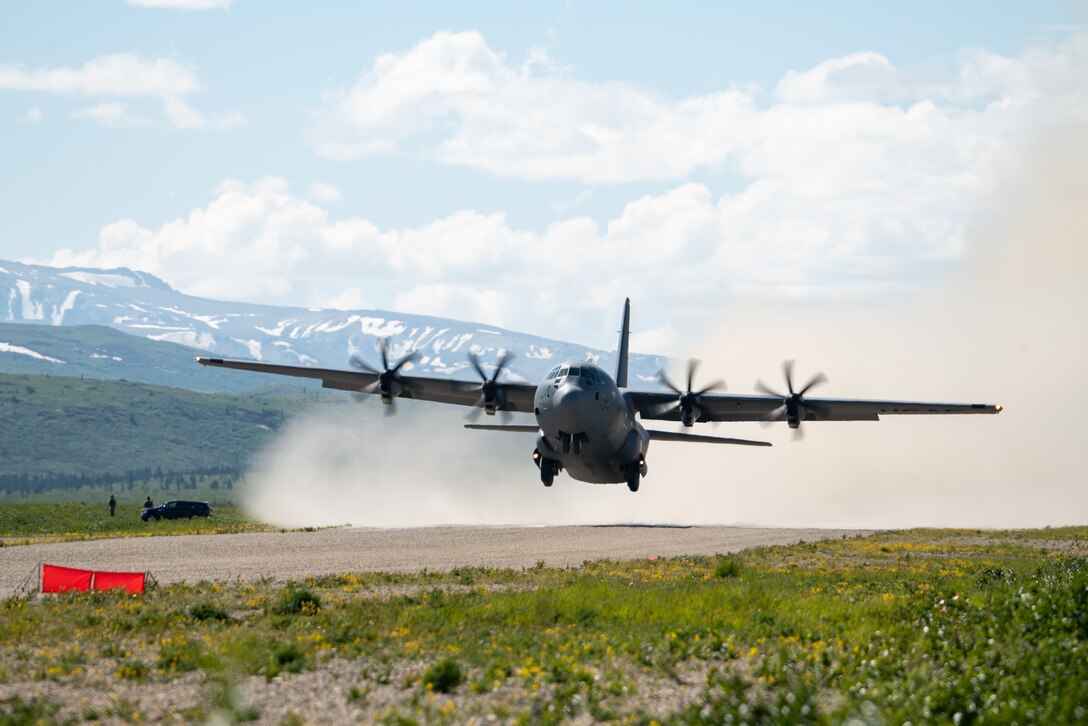 A C-130 lifts up off of a dirt runway.