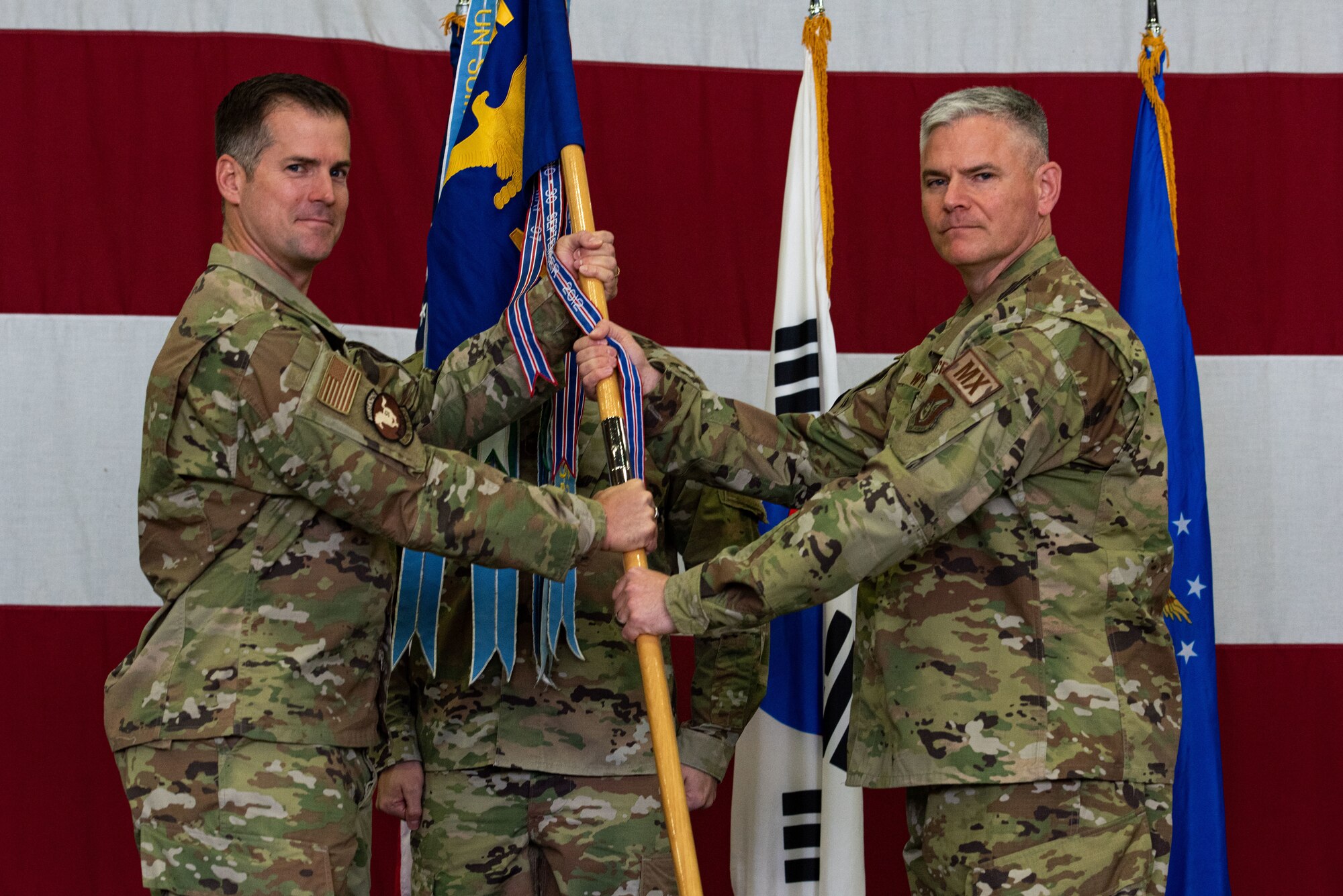 Col. Joshua Wood, 51st Fighter Wing commander, left, passes the guidon to Col. Todd Wydra, 51st Maintenance Group incoming commander, as a symbol of his taking command of the MXG at Osan Air Base, Republic of Korea, June 15, 2022.