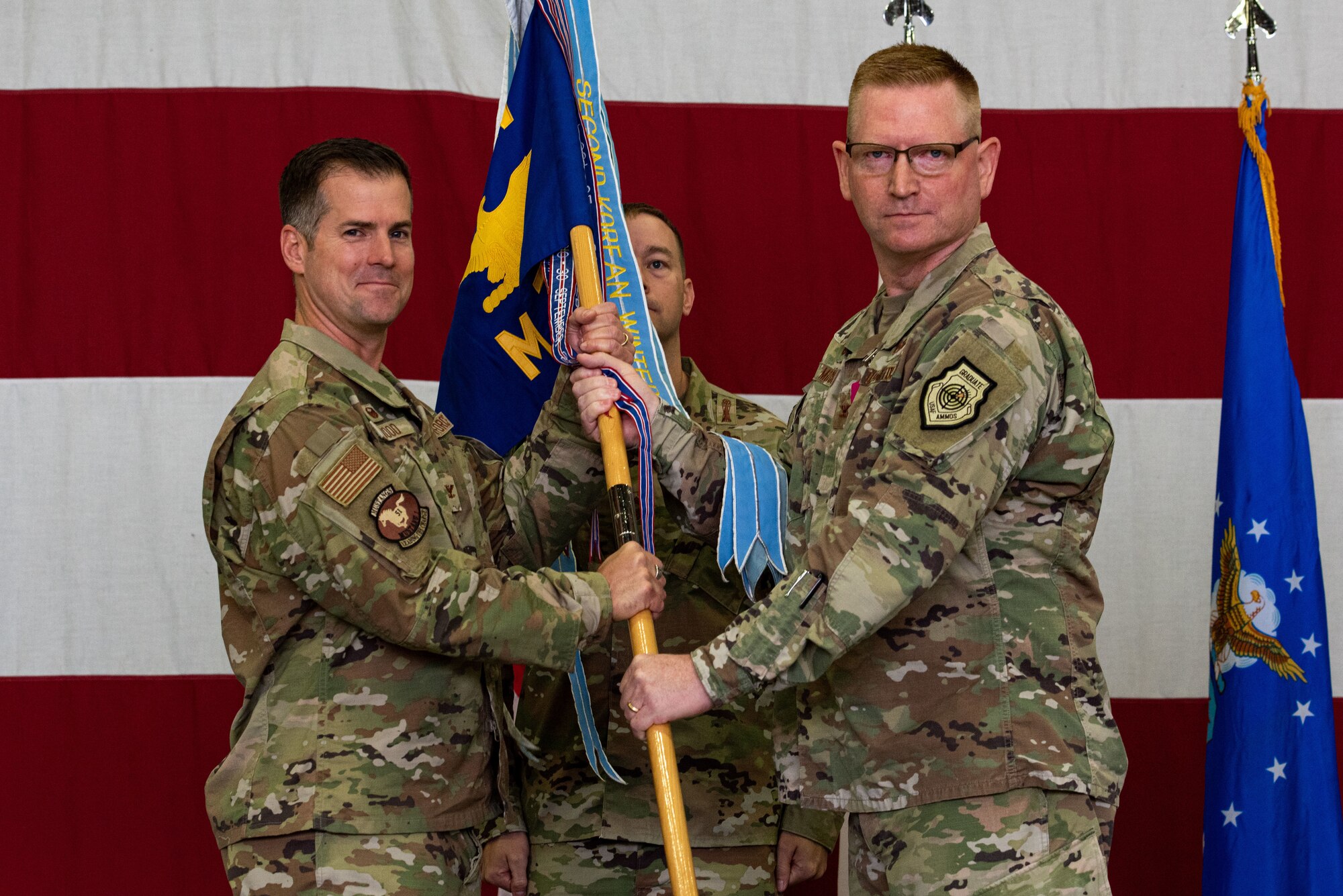 Col. Joshua Wood, 51st Fighter Wing commander, left, receives the guidon from Col. Brian Moore, 51st Maintenance Group outgoing commander, as a symbol of his relinquishment of command of the MXG at Osan Air Base, Republic of Korea, June 15, 2022.