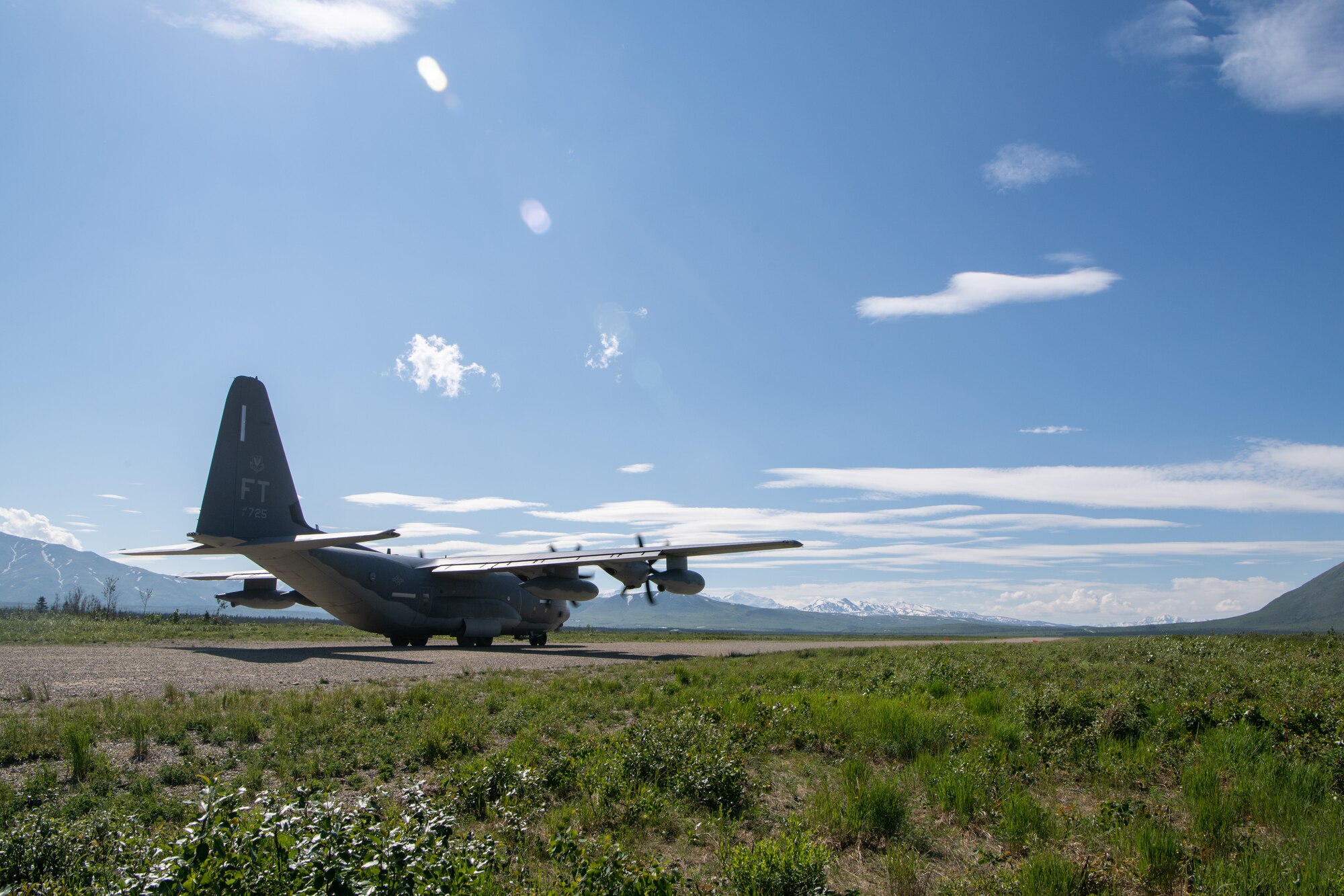 A C-130 sits at the end of a dirt strip runway.
