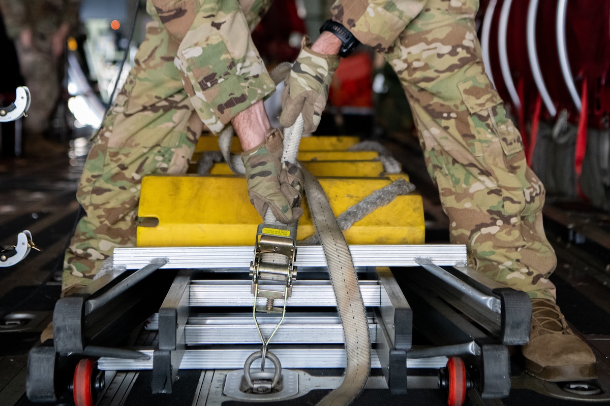An Airman uses a ratchet strap to secure cargo in the back of a plane.