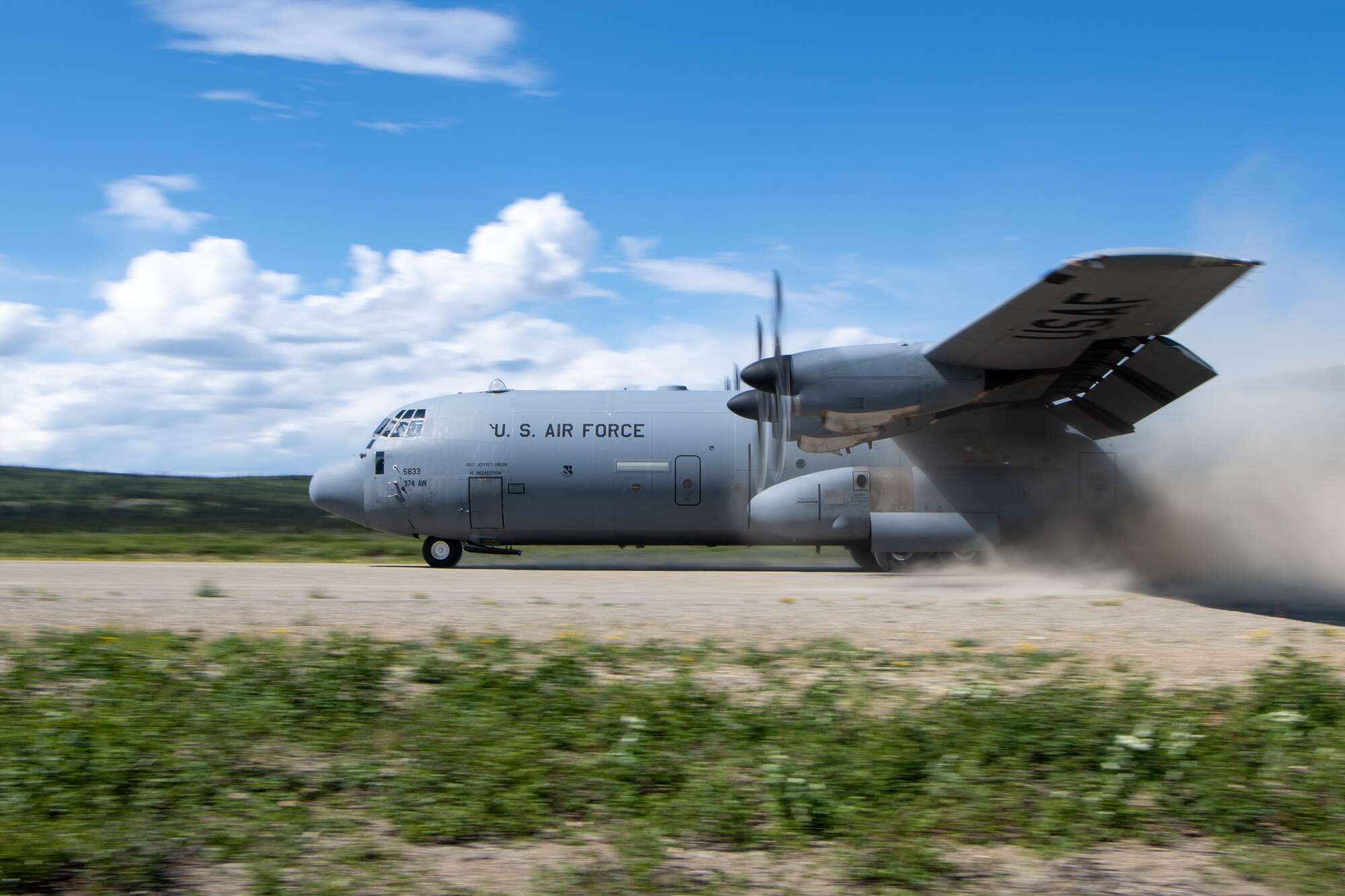 A C-130 take off from a dirt runway.
