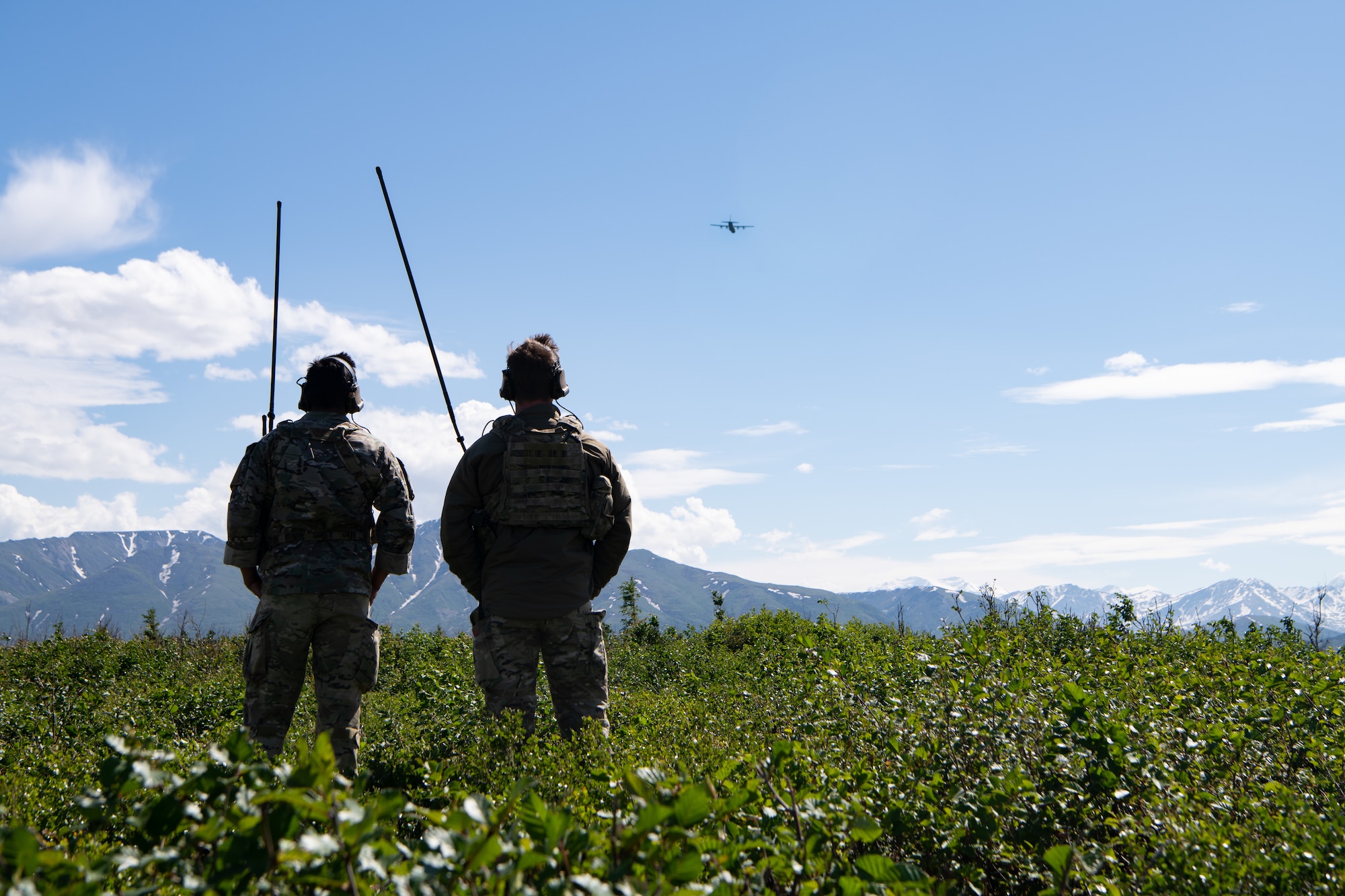 Two men observe a C-130 flying away.