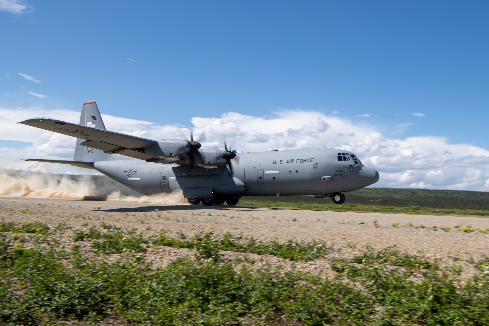 A C-130 takes off from a dirt runway.