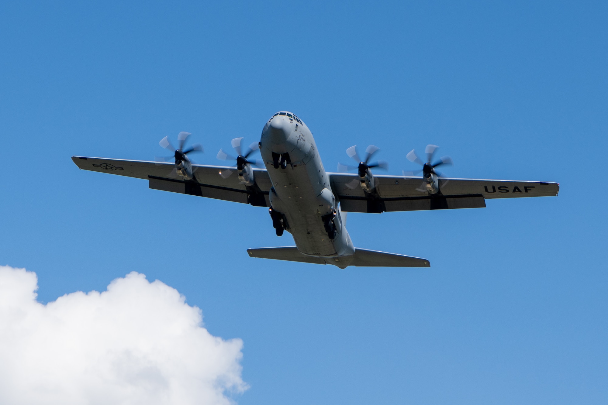 A C-130 flies against a clear blue sky.