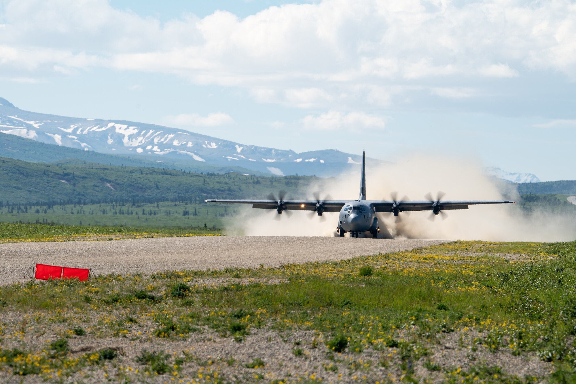 A C-130 takes off from a dirt runway.