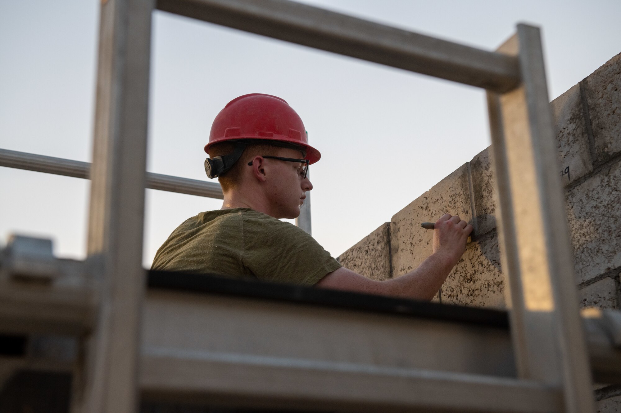 U.S. Air Force Senior Airman Ethan King, a structural journeyman with the 1st Civil Engineer Group, marks a wall for the placement of rebar during a construction project on Al Udeid Air Base, Qatar, June 15, 2022. Rebar is placed within the masonry bricks, which are then filled with concrete in order to fully reinforce the structure. (U.S. Air National Guard photo by Airman 1st Class Constantine Bambakidis)