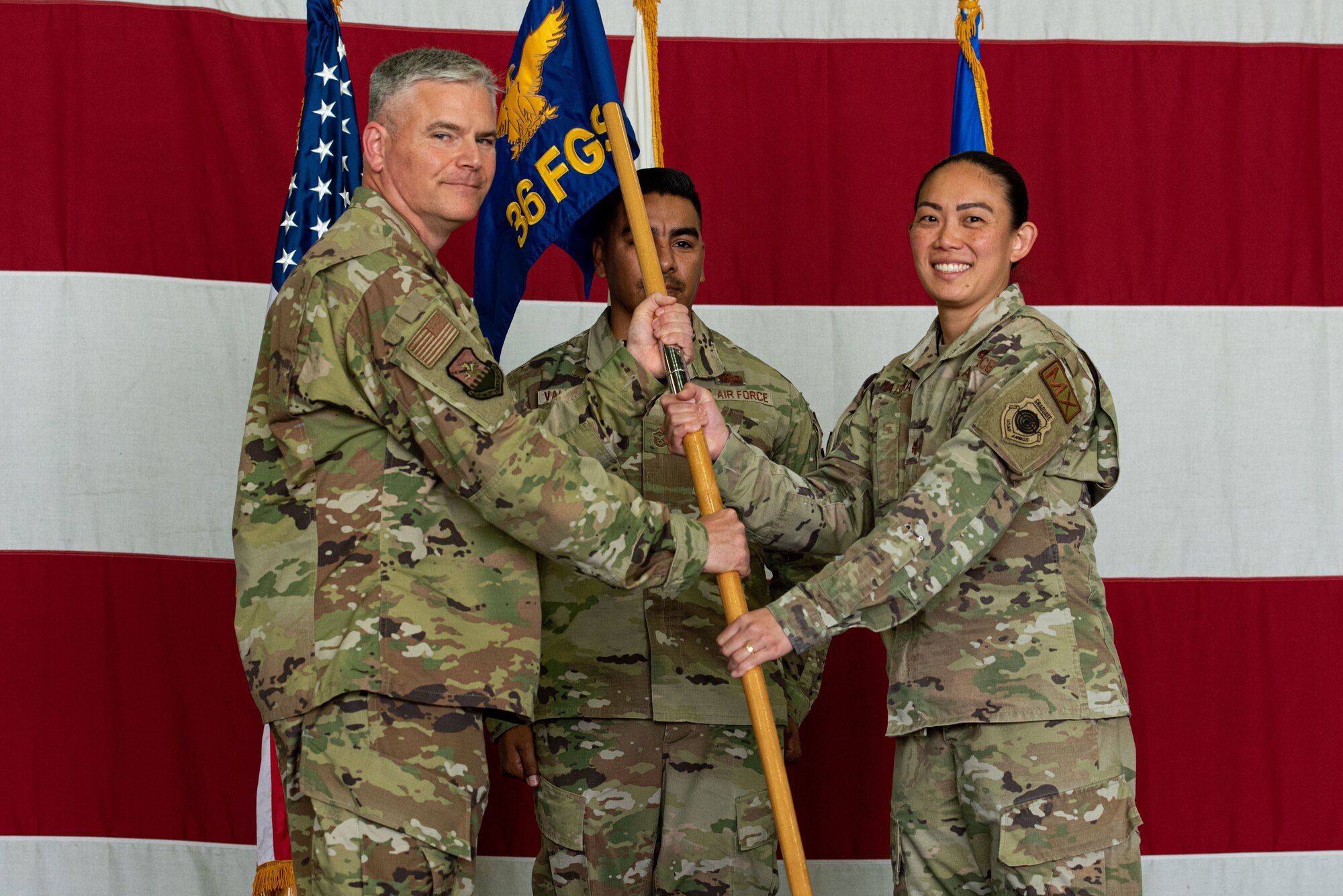 Col. Todd Wydra, 51st Maintenance Group commander, left, passes the squadron flag to Maj. Kelliane Matsuoka, 36th Fighter Generation Squadron commander