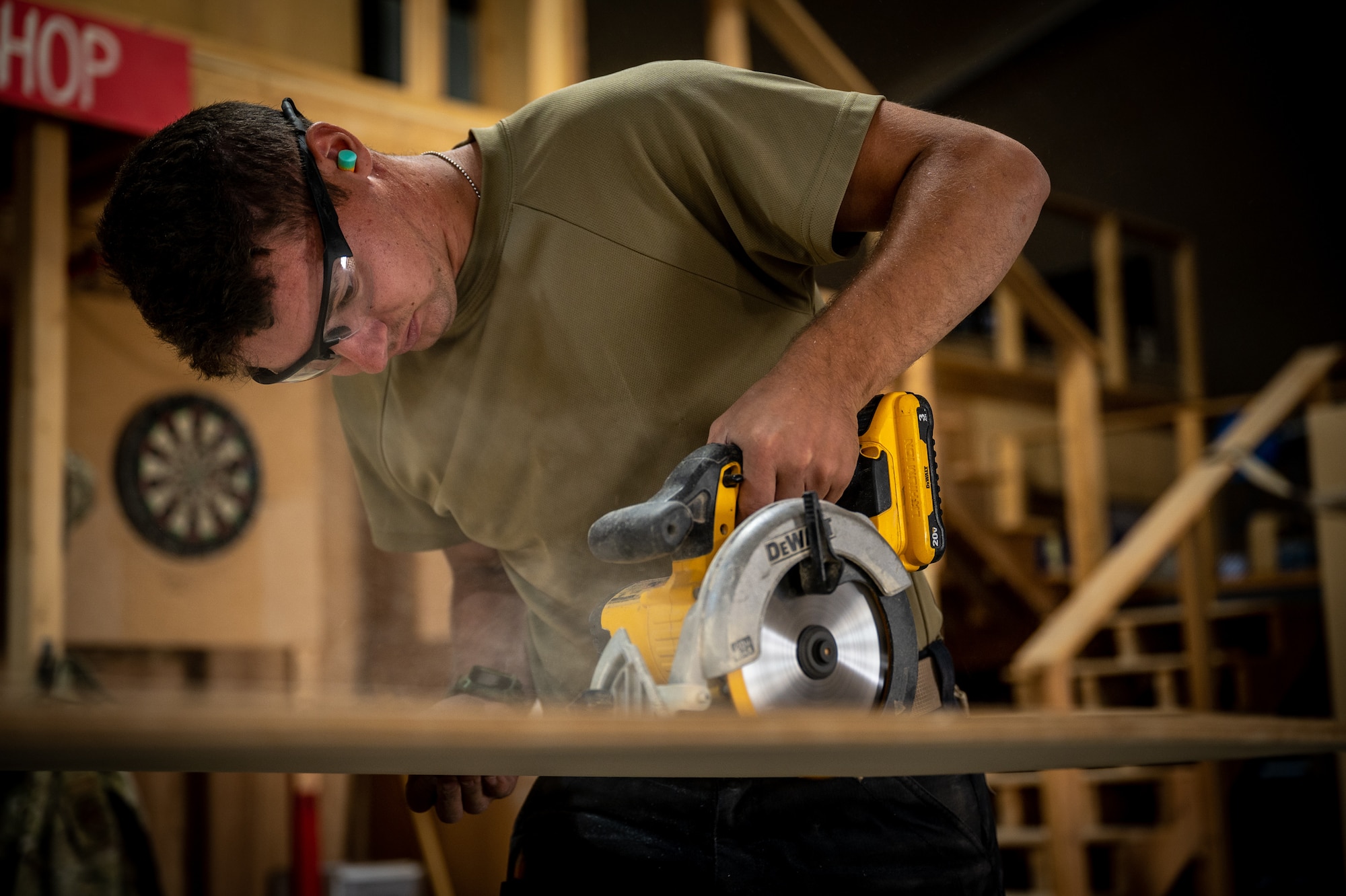 Airman First Class Bryson Doll, 332d Expeditionary Civil Engineer Squadron structural apprentice, uses a circular saw to cut wood that will be used to craft a challenge coin holder at an undisclosed location in Southwest Asia, May 21, 2022. During his deployment, Doll has volunteered 50 hours, before and after work, on various woodworking projects that include bag toss boards, a bench crafted from a shipping palate, a picnic table, a tail fin coin holder, and several other projects. (U.S. Air Force photo by Master Sgt. Christopher Parr)