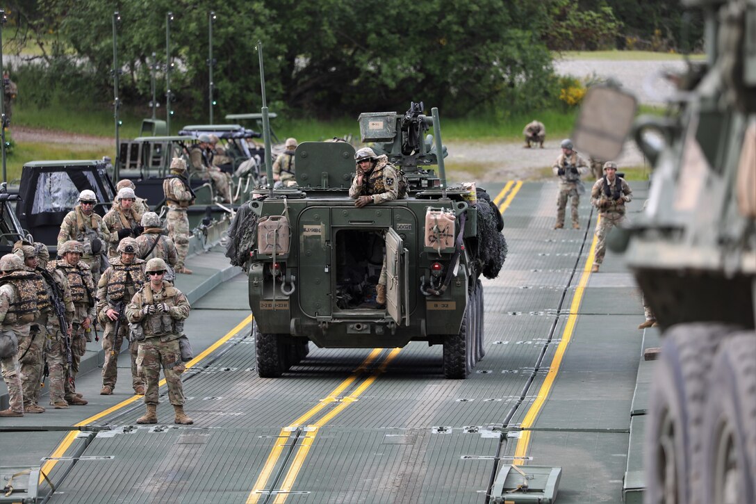 Soldiers and armored vehicles cross a bridge.