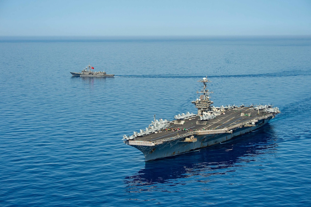 An aircraft carrier and a smaller ship transit close to each other.