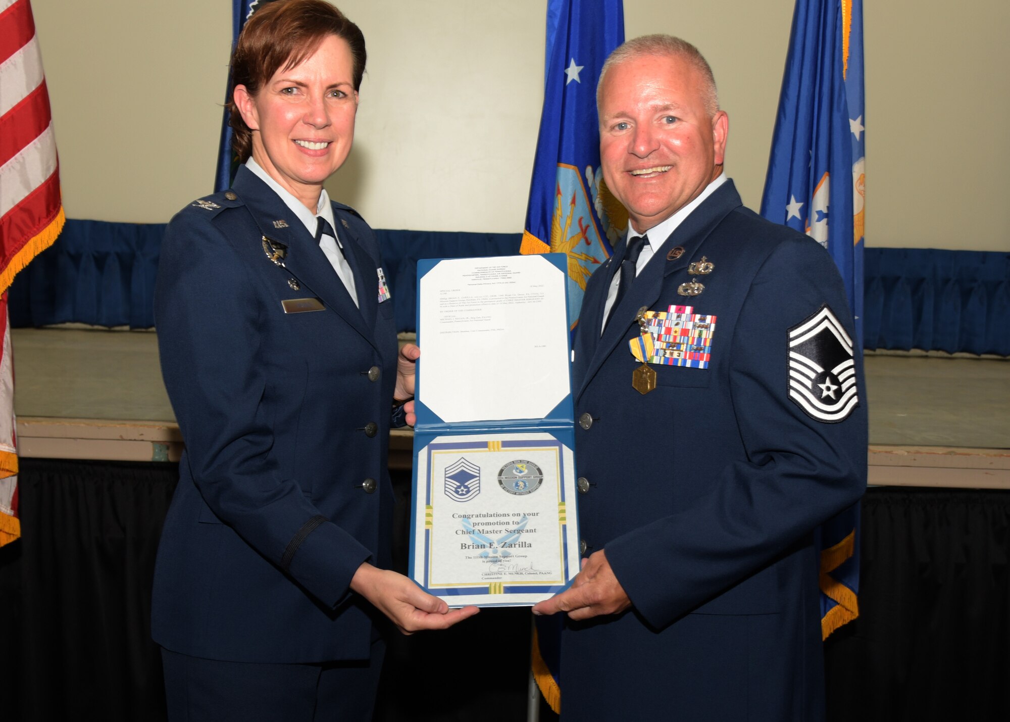 Two military personnel in uniform holding a certificate of promotion.