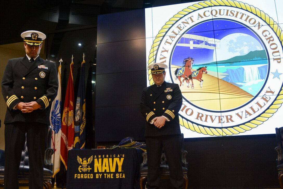 Two men in US Navy uniforms bow their heads on stage.