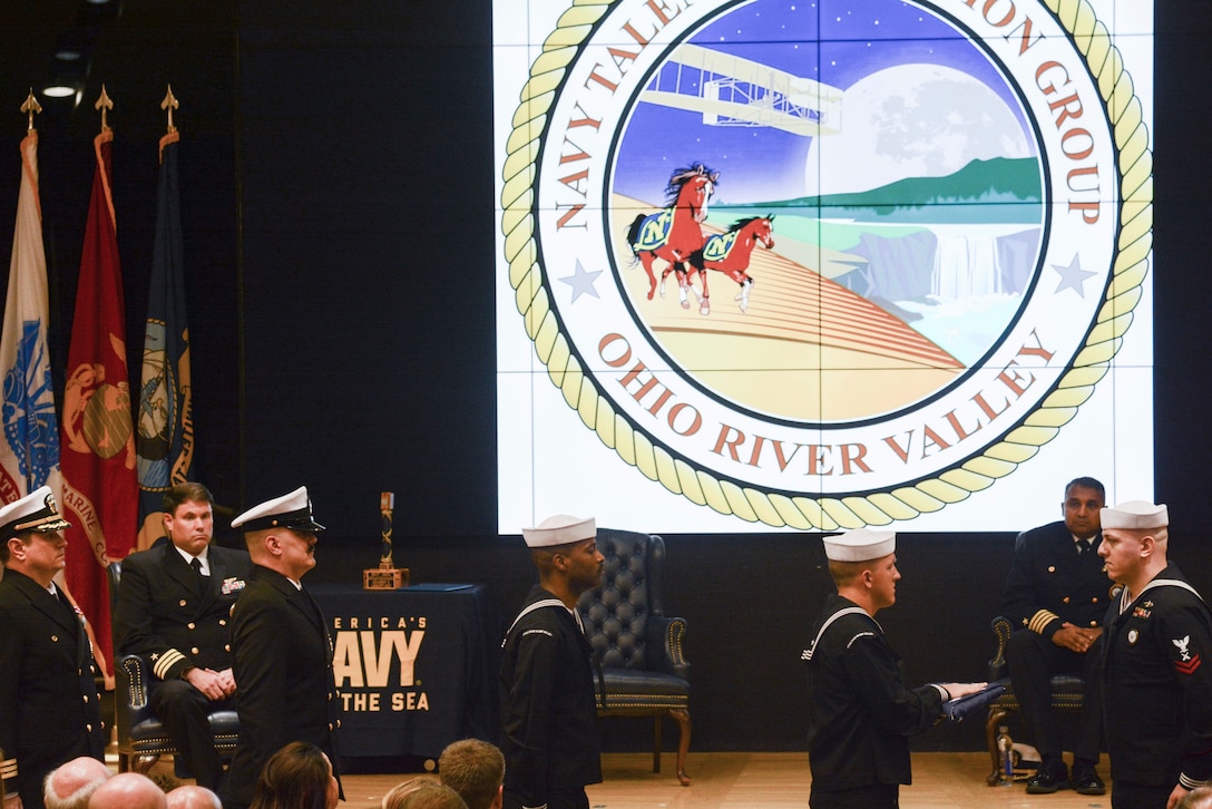 Several people in US Navy uniforms in an auditorium for a ceremony