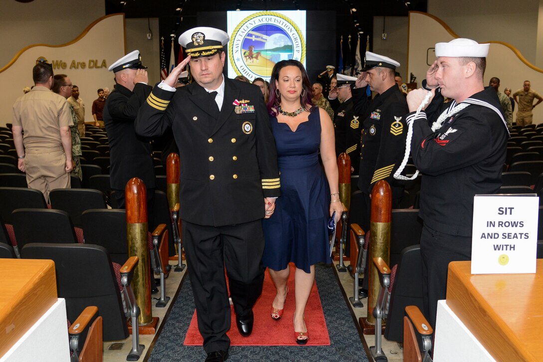 Man in Navy uniform with a woman in a blue formal dress walk down the aisle at the end of a ceremony.