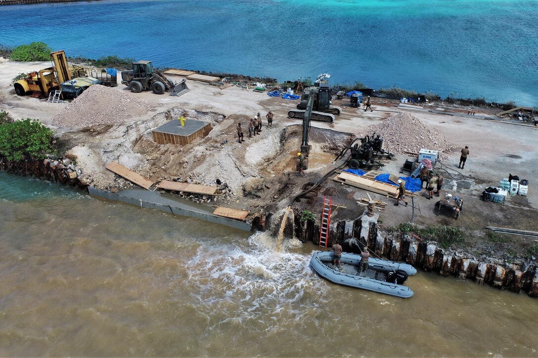 Sailors use equipment to do construction work on a harbor.