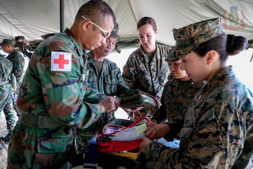 Military medical personnel open gear beneath a tent.