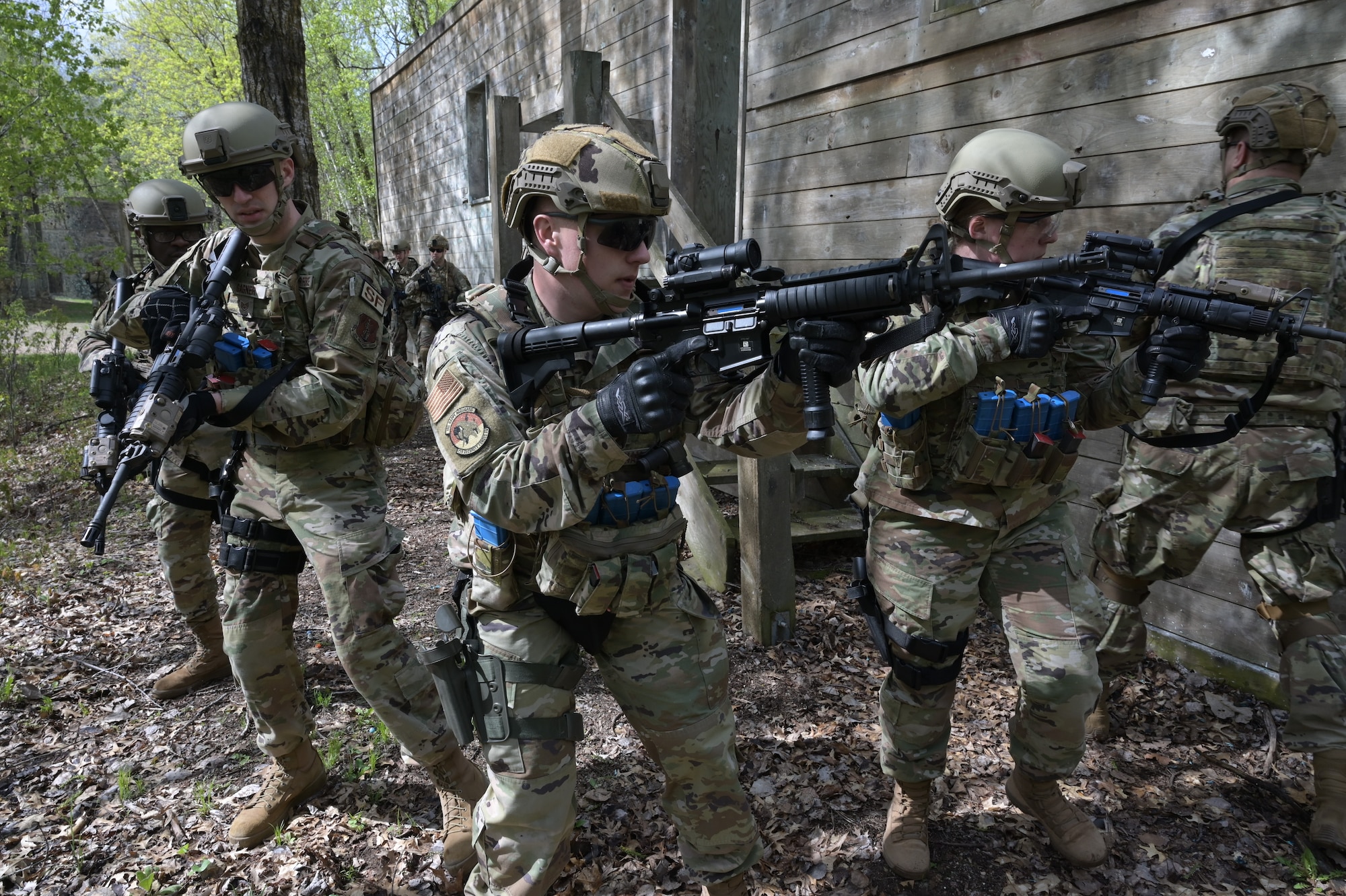 A group of 119th Security Forces Squadron members in military uniforms carry M4 rifles loaded with simulated ammunition as they perform training in a mock building.