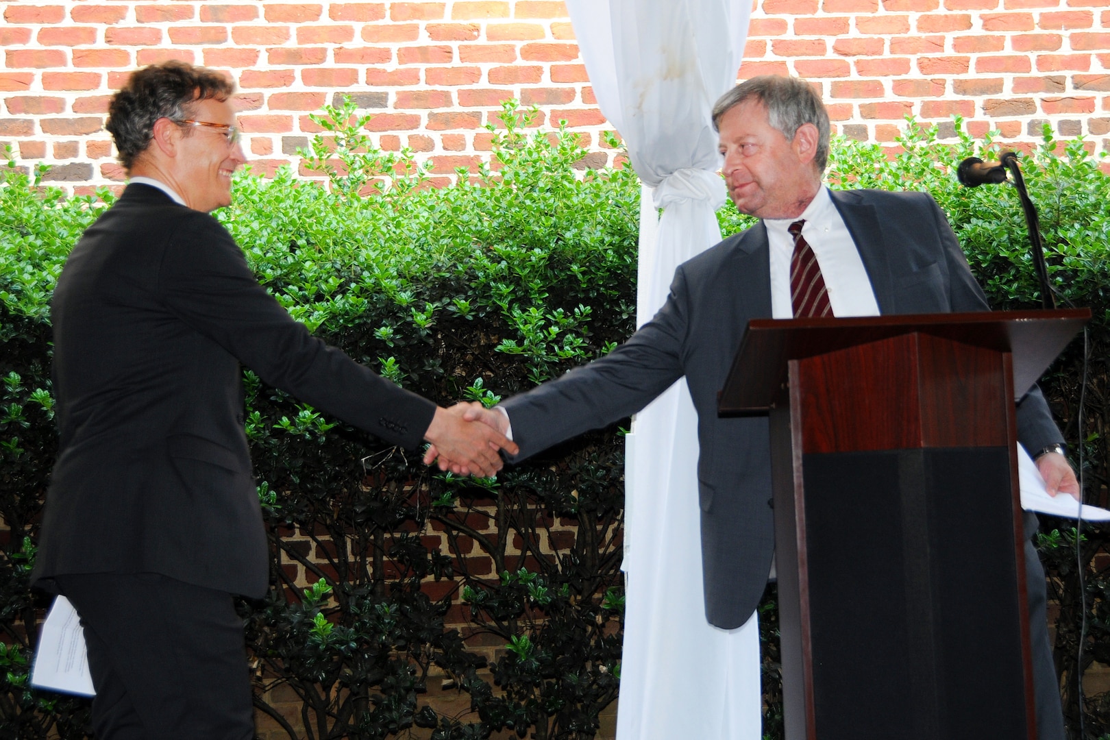 Two men shake hands behind a lectern.
