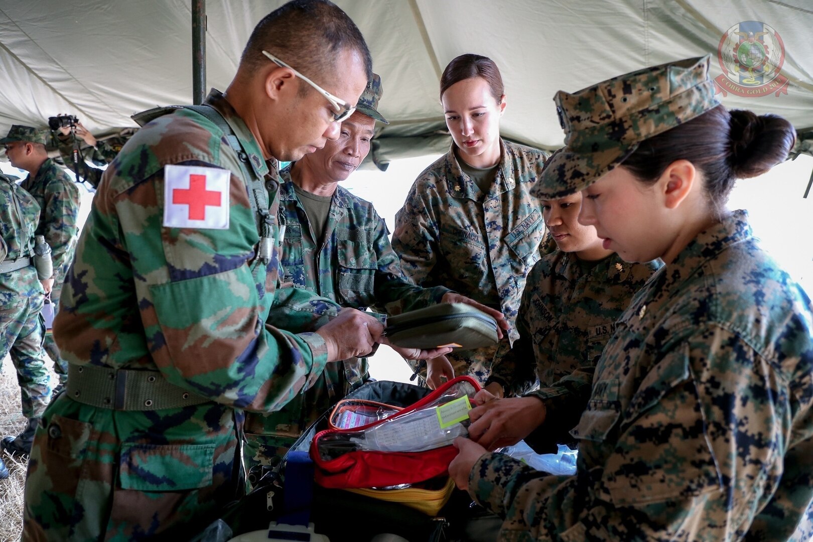 Military medical personnel open gear beneath a tent.