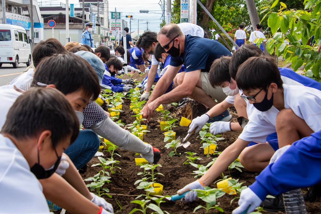 A group of people garden along a sidewalk.