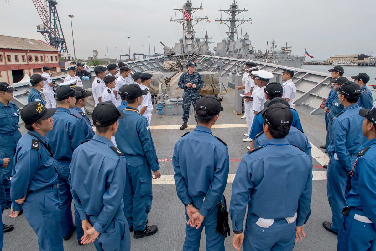 Military personnel gather around a U.S. sailor on the deck of a military vessel.