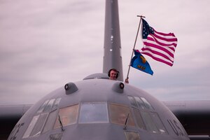 Senior Airman Isaac McMullen, 96th Airlift Squadron loadmaster, waves the American flag and Maintenance Group guidon as his C-130H Hercules returns from a three-month deployment to Europe on May 19, 2022, at Minneapolis-St. Paul Air Reserve Station. The 934th Airlift Wing performed tactical airlifts and vital aeromedical evacuations in support of U.S. European Command to assure our Allies and Partners in the region and deter any future aggression. (U.S. Air Force Picture by Chris Farley)