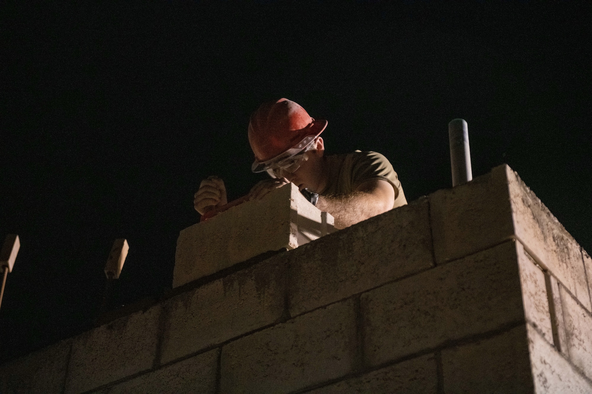 U.S. Air Force Staff Sgt. Stephen Bartlett, a structural journeyman with the 1st Expeditionary Civil Engineer Group, sets a concrete masonry unit in place during a construction project on Al Udeid Air Base, Qatar, June 17, 2022. 1 ECEG has been constructing a splinter-protected laundry, shower, and latrine facility on the flight line. (U.S. Air National Guard photo by Airman 1st Class Constantine Bambakidis)