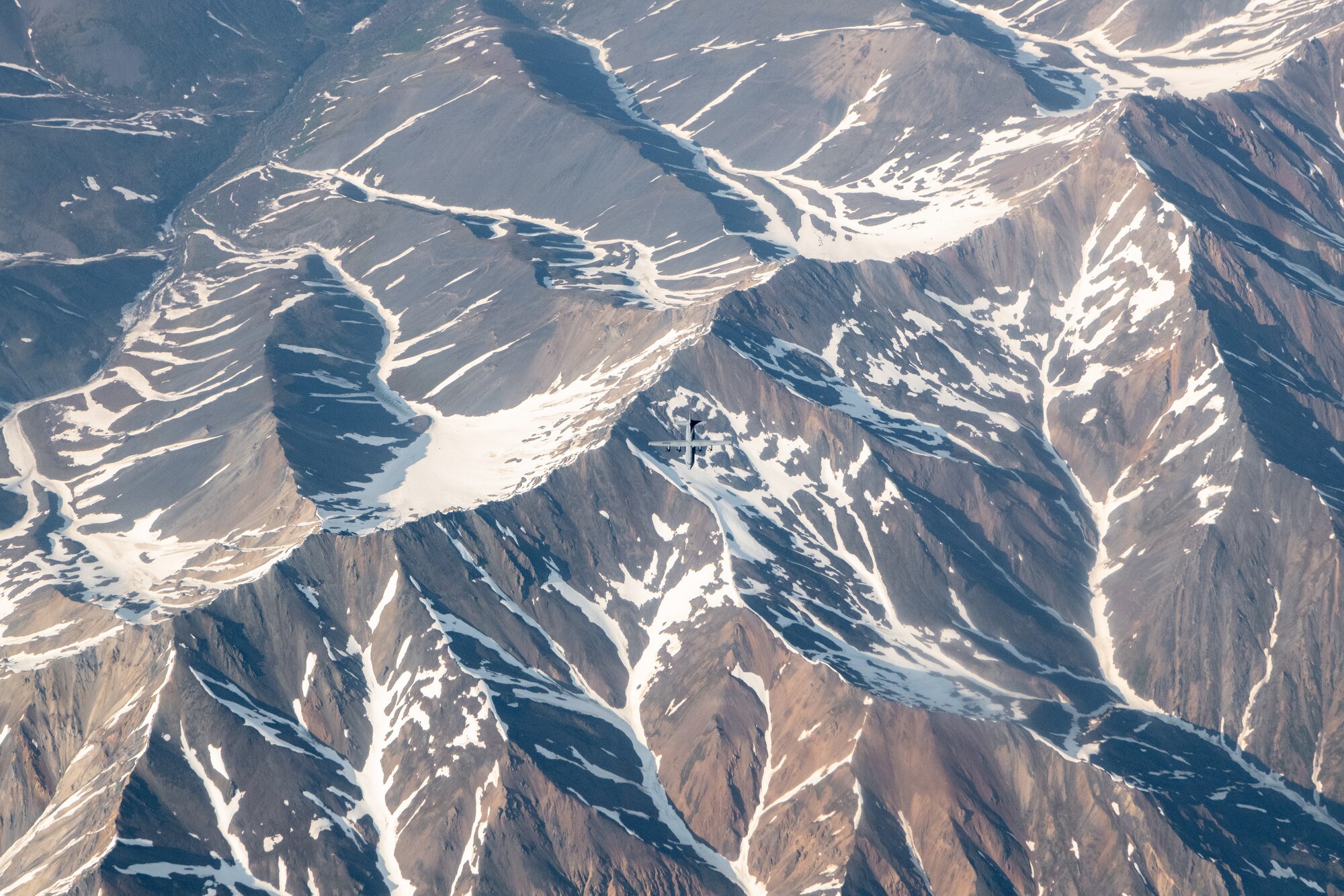 A C-130 flies above a mountain range.