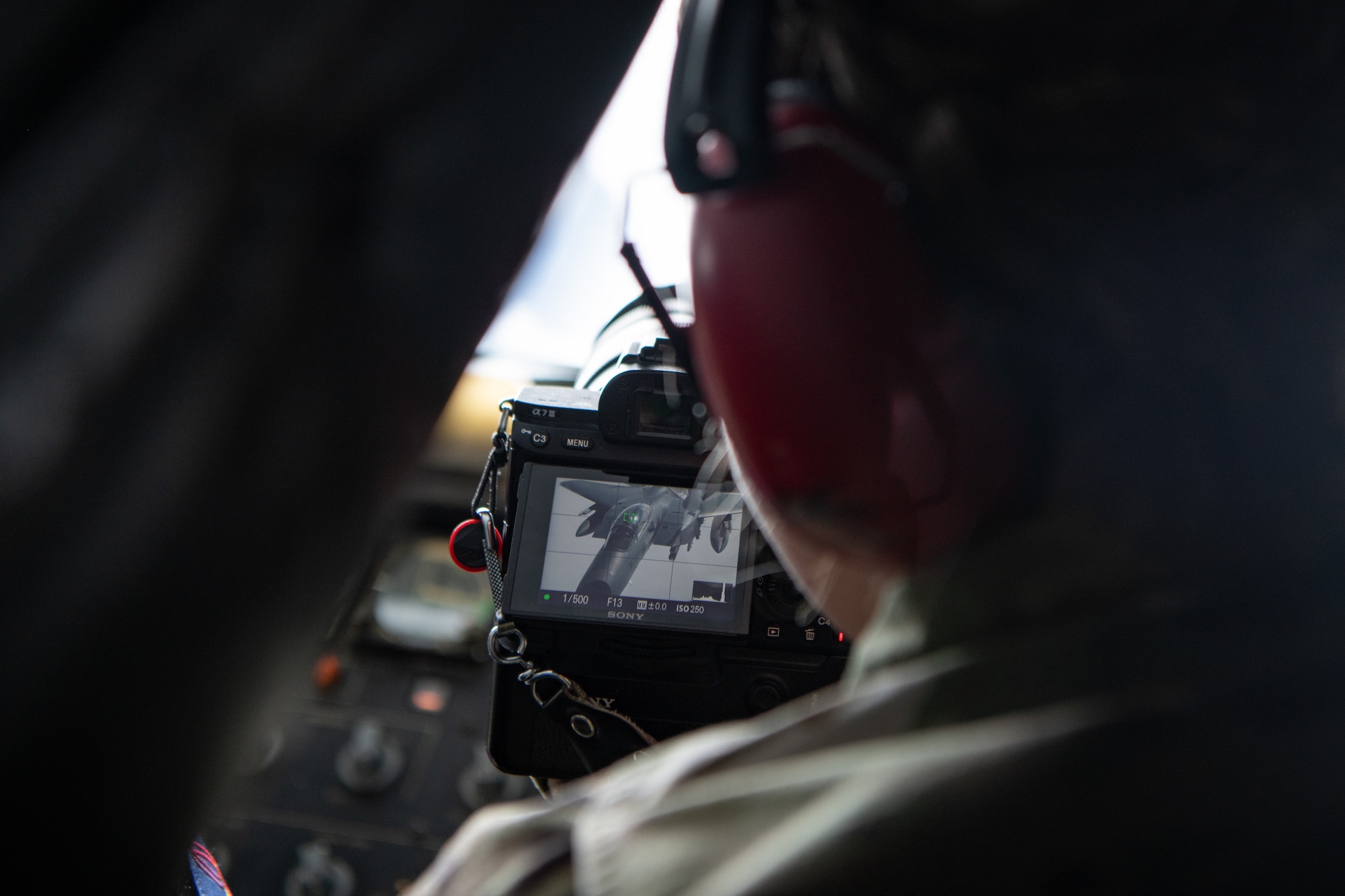 An airman holds a camera, showing a jet on the screen.