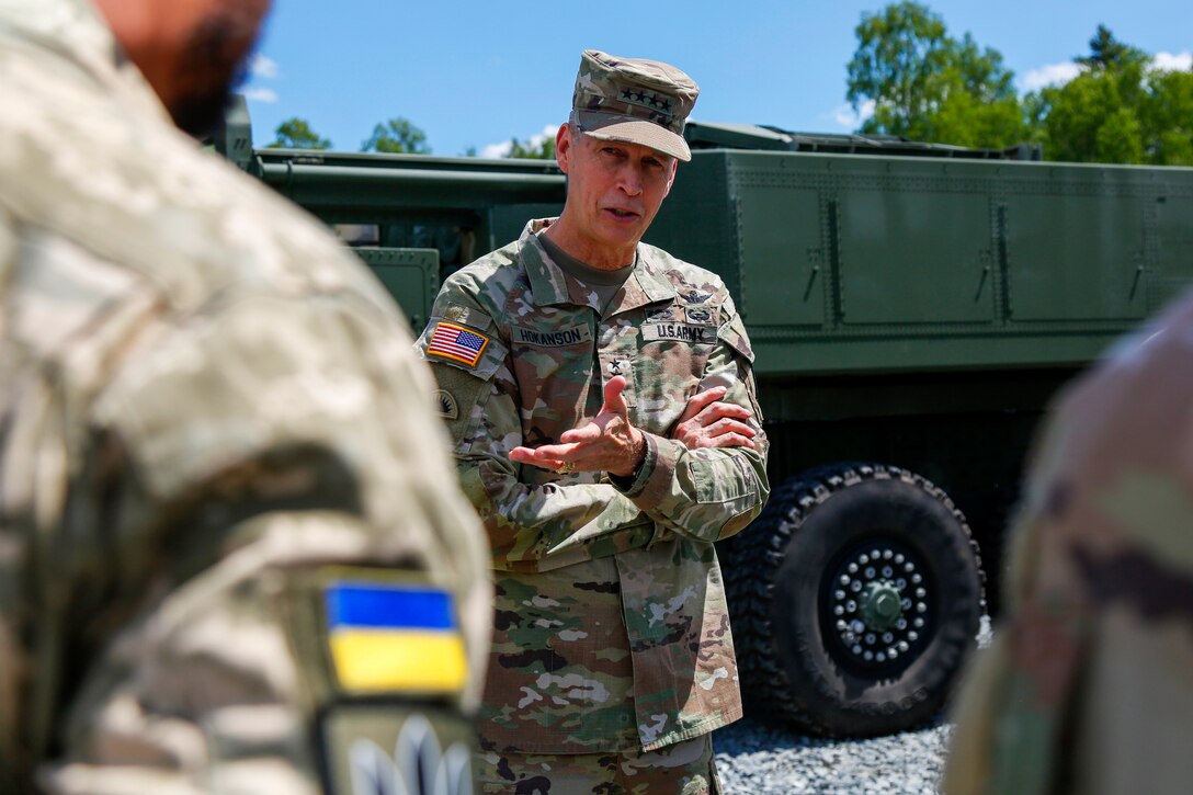 An Army officer talks with service members while standing next to a military vehicle.